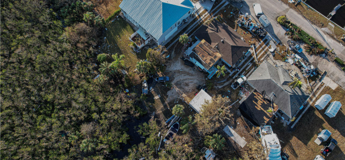Aerial view of hurricane-damaged Florida neighborhood with homes lacking storm shutters and widespread debris